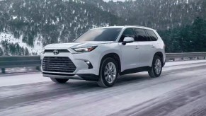 A white 2024 Toyota Grand Highlander Hybrid is driving on a snowy road.