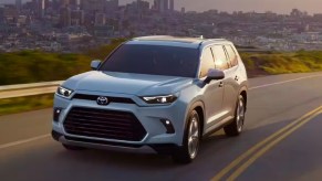 A white 2024 Toyota Gand Highlander Hybrid midsize three-row hybrid SUV is driving on the road.