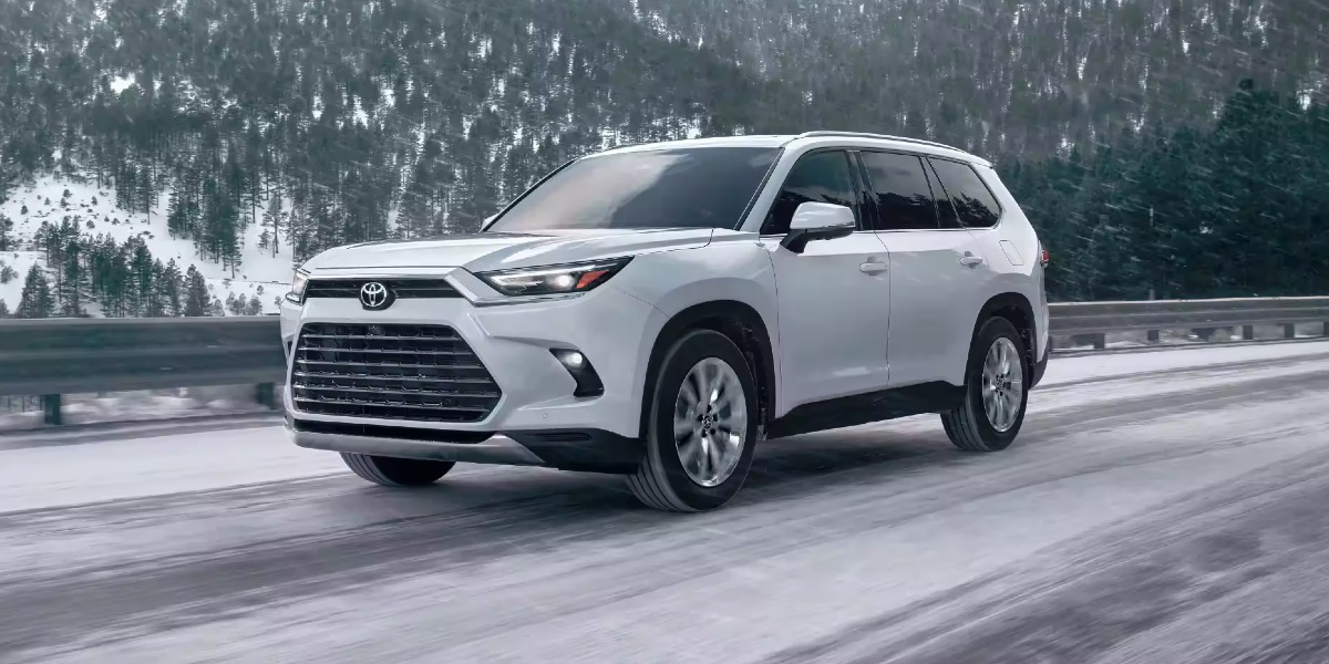 A white 2024 Toyota Grand Highlander midsize three-row SUV is driving on a snowy road.