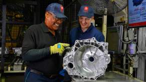 A Toyota Motor North America promo photo of two smiling workers standing over a car part