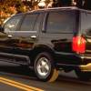 A black 1998 Lincoln Navigator full-size luxury SUV model driving past bushes as the sun sets