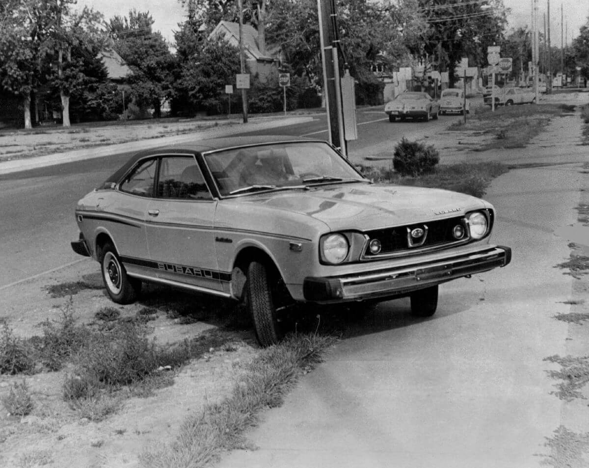 A Loyale predecessor, a Subaru GI Coupe model, parked on the grass and sidewalk