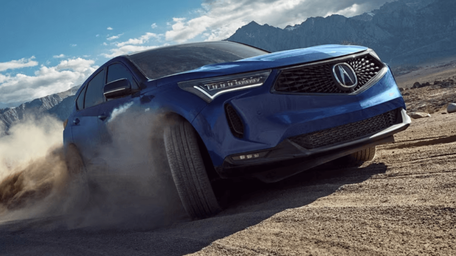 A 2024 Acura RDX compact luxury SUV model driving on off-road dirt as its tires spin up dust clouds