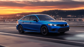 A 2024 Honda Civic Si sports sedan in Aegean Blue Metallic on a highway as the sun sets over a city