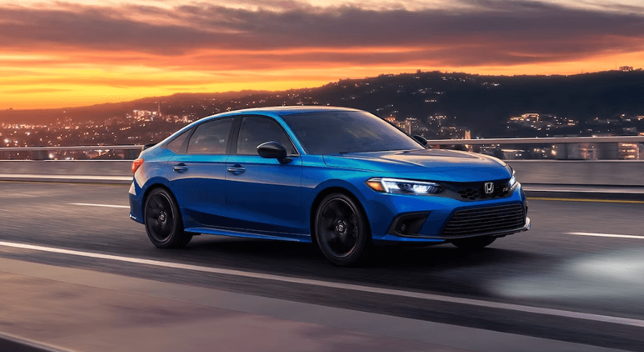 A 2024 Honda Civic Si sports sedan in Aegean Blue Metallic on a highway as the sun sets over a city