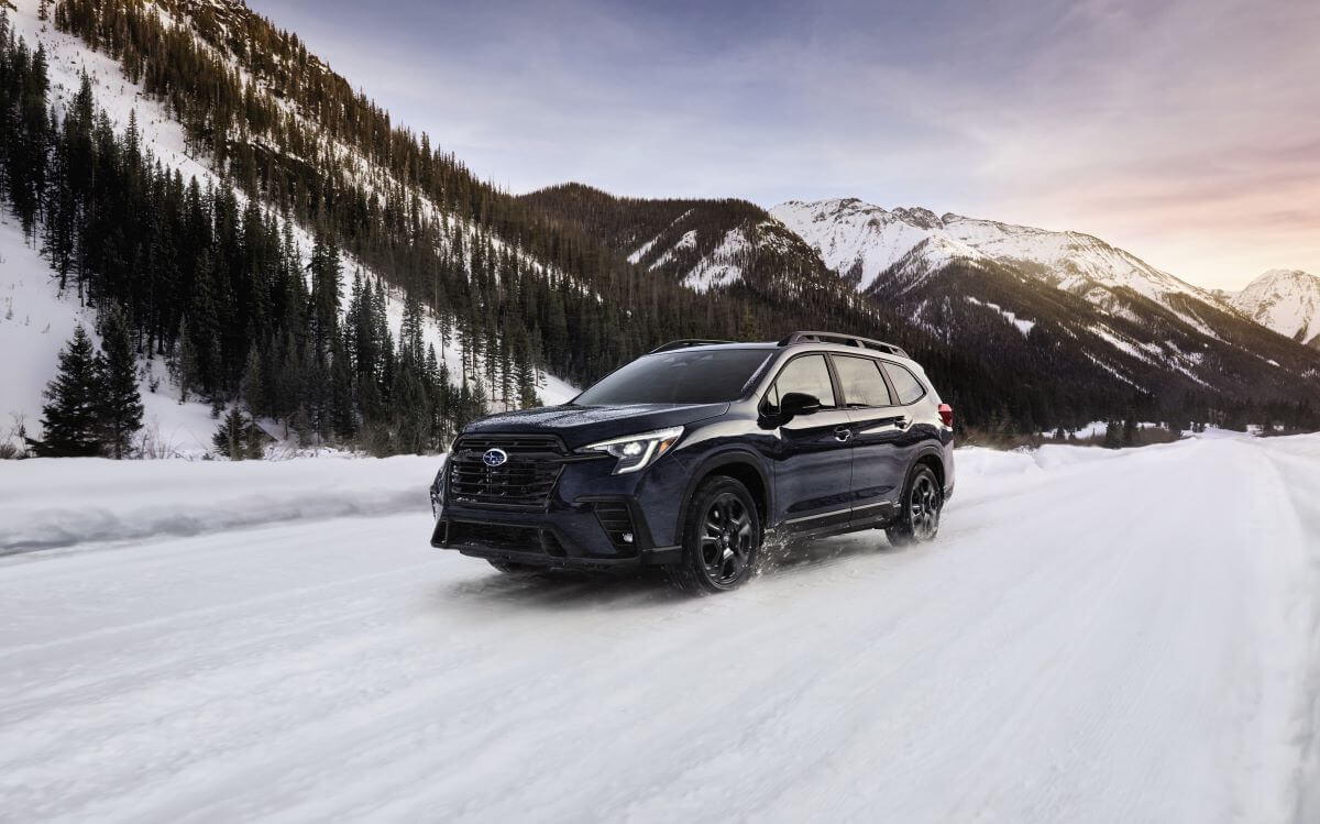 A 2024 Subaru Ascent midsize SUV model with roof rails driving through the snow in a mountain of forests
