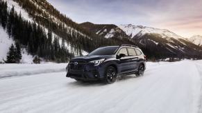 A 2024 Subaru Ascent midsize SUV model with roof rails driving through the snow in a mountain of forests