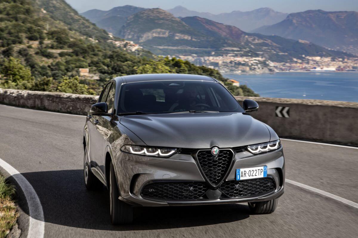 A 2024 Alfa Romeo Tonale plug-in hybrid compact SUV model driving on a scenic highway near seaside towns