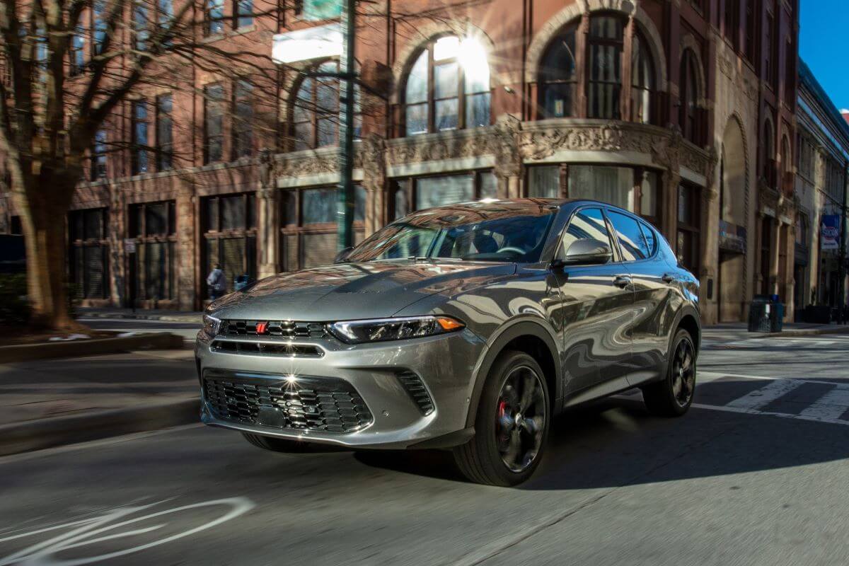 A 2024 Dodge Hornet GT performance-oriented compact SUV model driving through a city past a crosswalk.