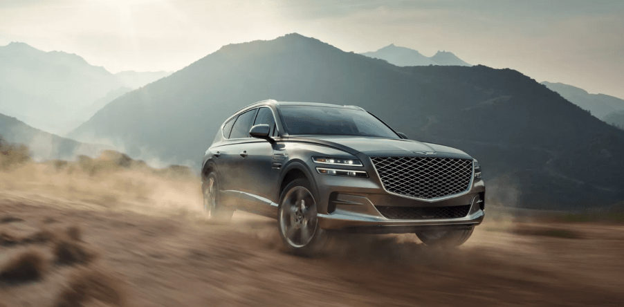 A 2024 Genesis GV80 midsize luxury all-electric SUV model driving off-road as dust kicks up in the mountains