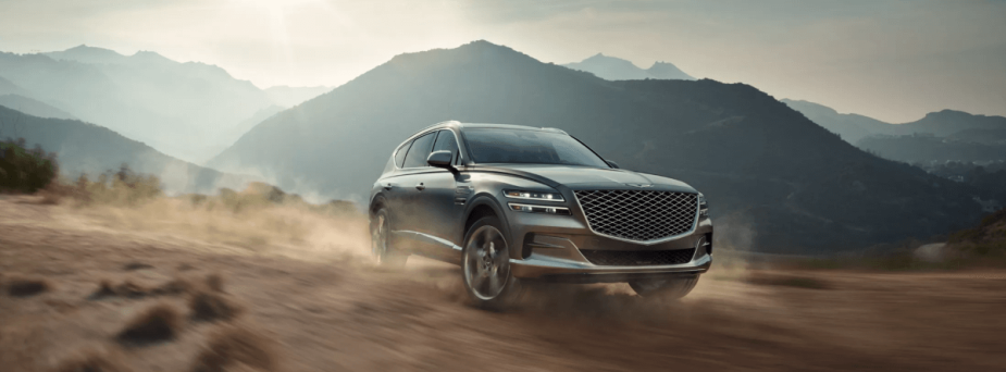 A 2024 Genesis GV80 midsize luxury all-electric SUV model driving off-road as dust kicks up in the mountains