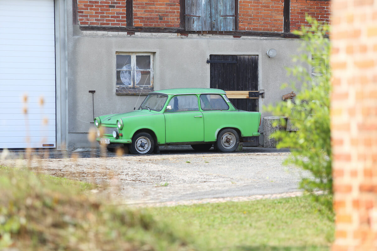 A green non-running car sits next to a building