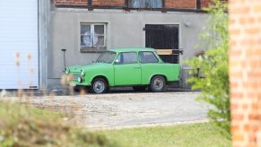 A green non-running car sits next to a building