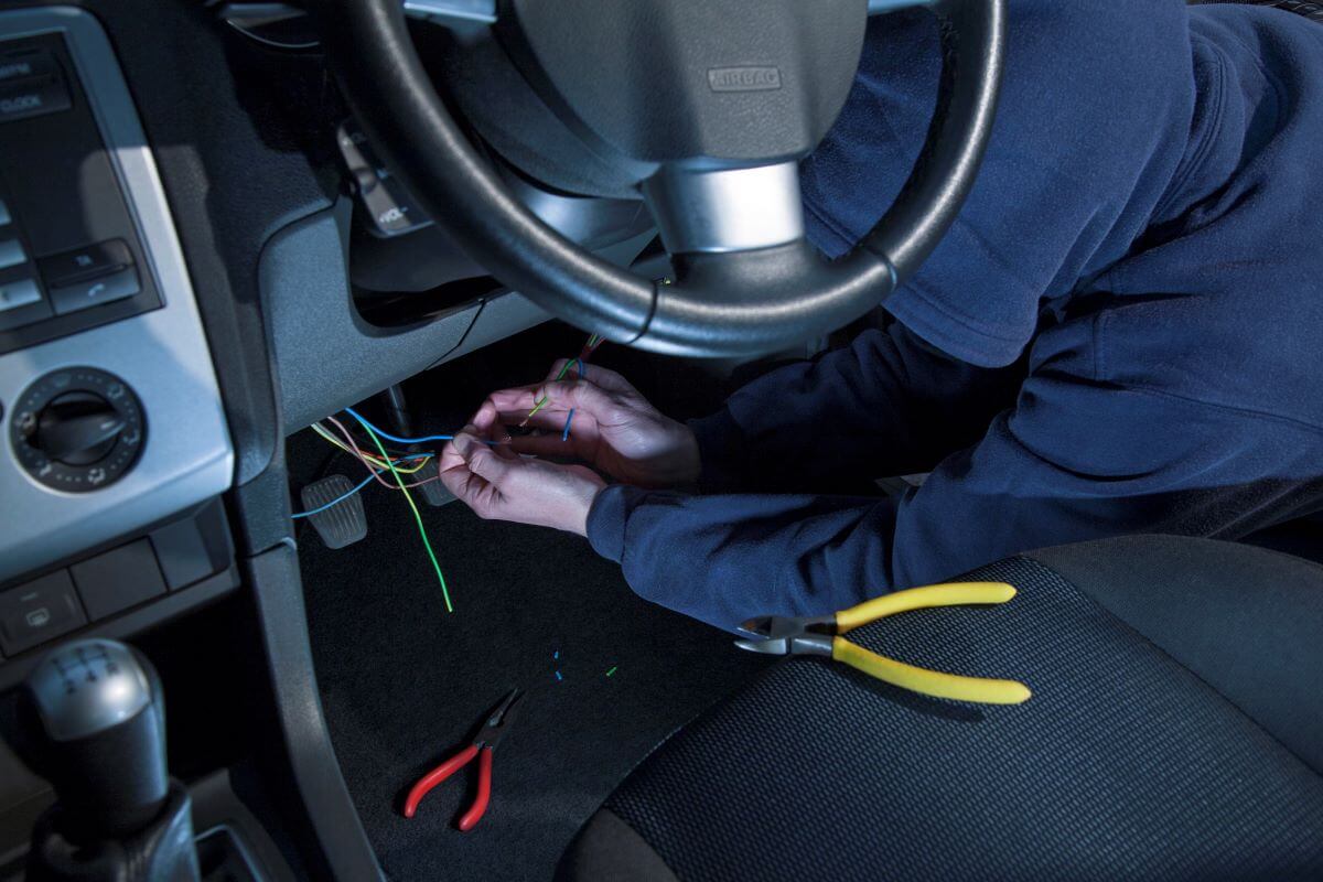 A man in black clothes and a hooded sweatshirt breaking into and hot wiring a car
