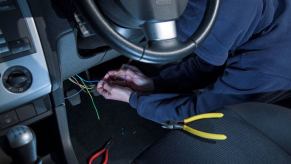 A man in black clothes and a hooded sweatshirt breaking into and hot wiring a car