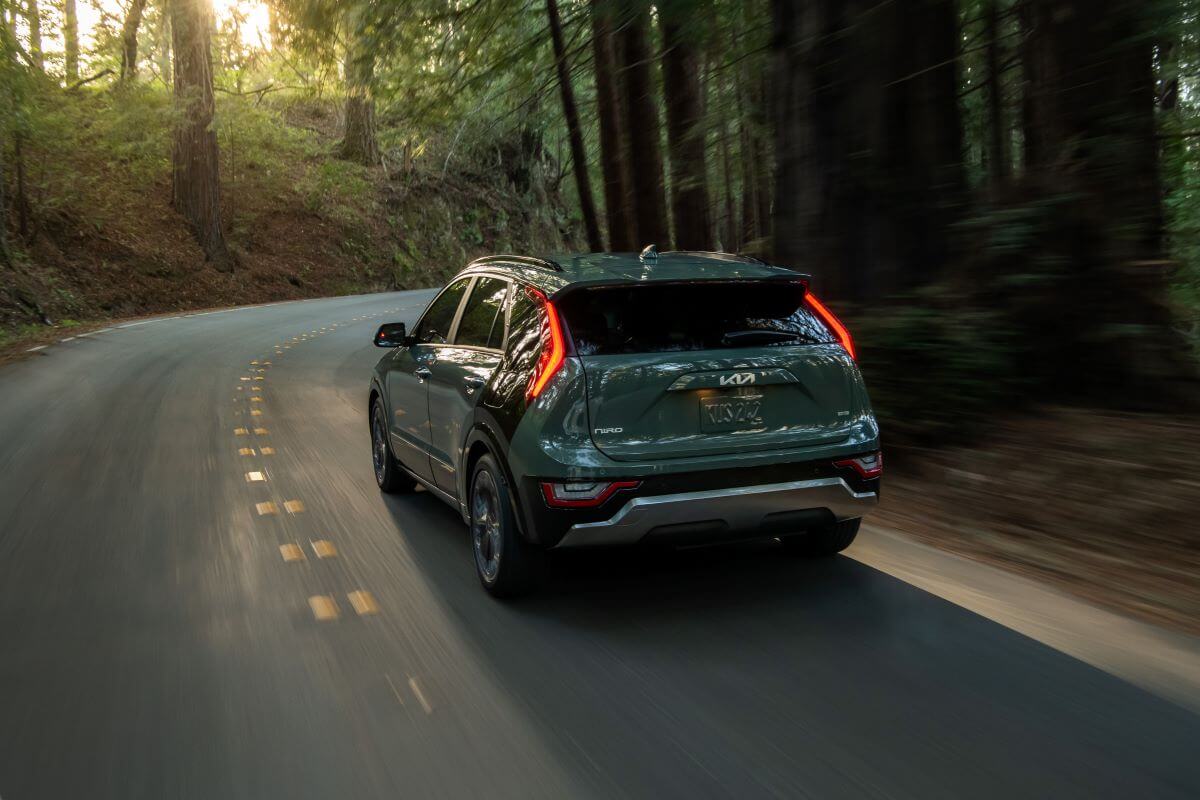 A 2023 Kia Niro compact hybrid SUV model driving on a forest road with its taillights lit up