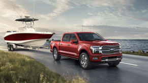 A 2024 Ford F-150 full-size pickup truck model towing a boat as it drive past a large lake of water