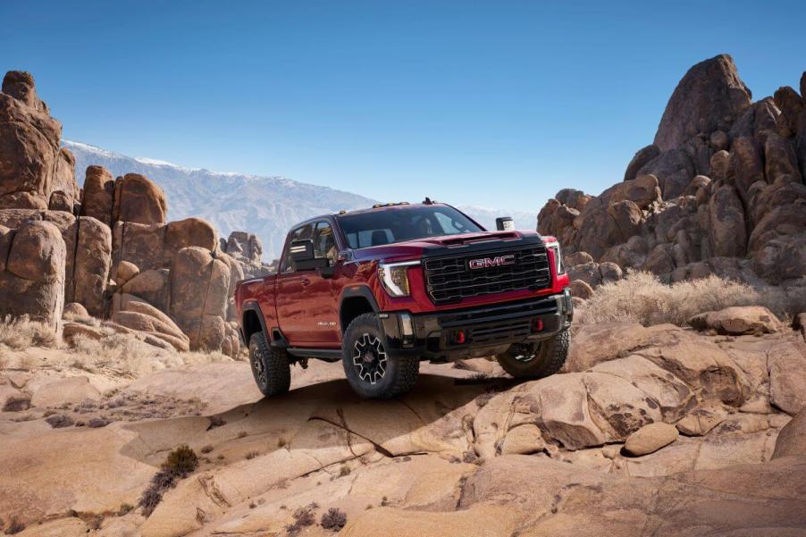 A 2024 GMC Sierra 2500 HD AT4X heavy-duty pickup truck model in Volcanic Red Tintcoat traveling off-road