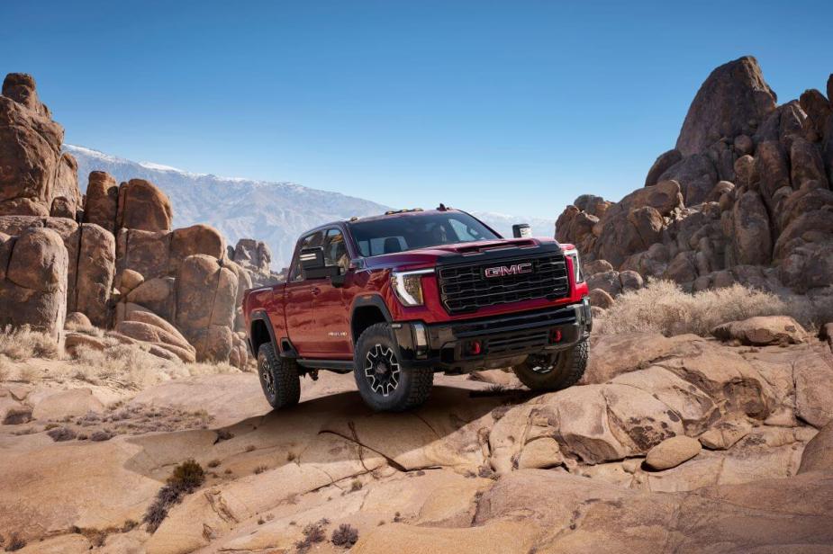 A 2024 GMC Sierra 2500 HD AT4X heavy-duty pickup truck model in Volcanic Red Tintcoat traveling off-road