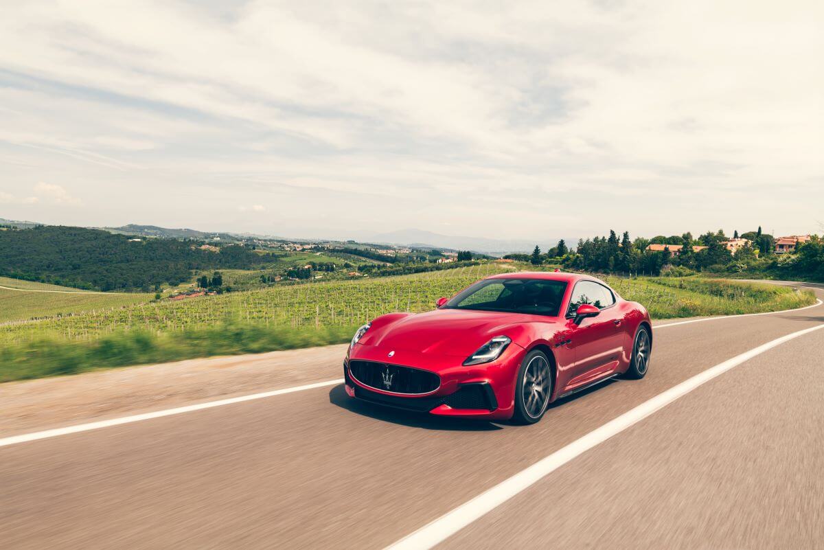 A 2024 Maserati GranTurismo Trofeo grand tourer model driving past farm houses and fields in Italy