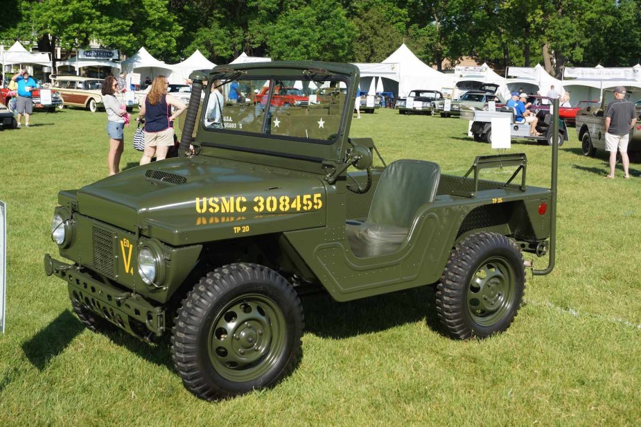 Dark green lightweight Mighty Mite compact military Jeep parked in a field during a car show.