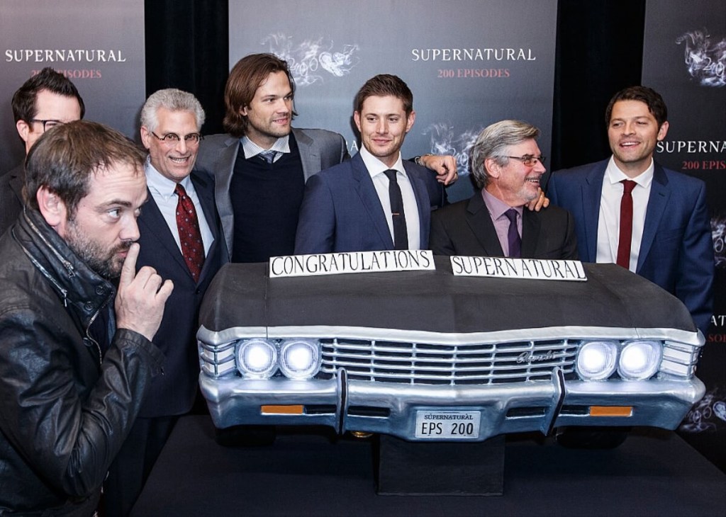 The crew and car of Supernatural, including Jensen Ackles as Dean Winchester, pose for a picture with a mock-up of a 1967 Chevy Impala.