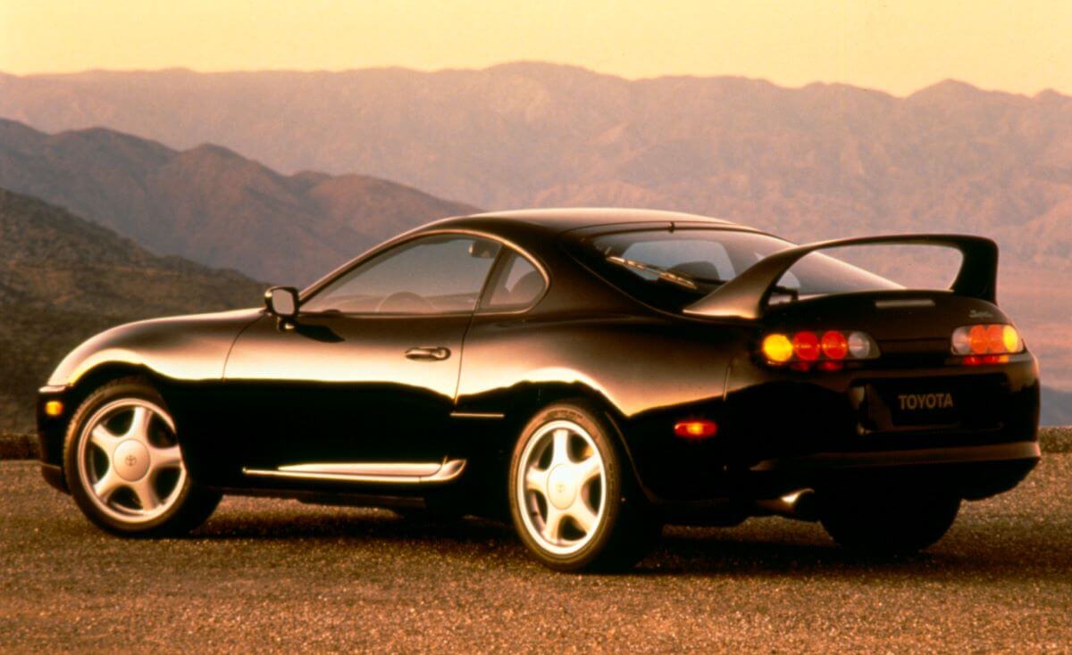 A rear/side profile shot of a 1994-1996 Toyota Supra sports car coupe model parked near a mountain range