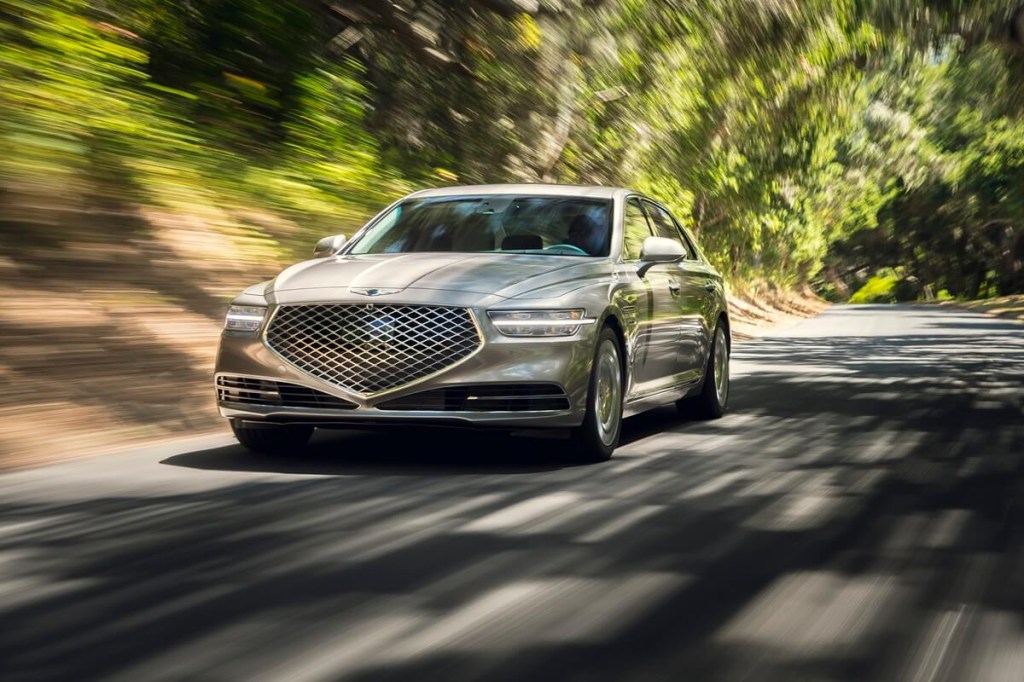 A used 2020 Genesis G90 luxury car drives through a forest.