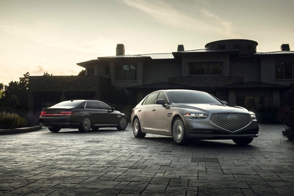 A set of used 2020 Genesis G90 luxury cars park on an apron next to a large home.