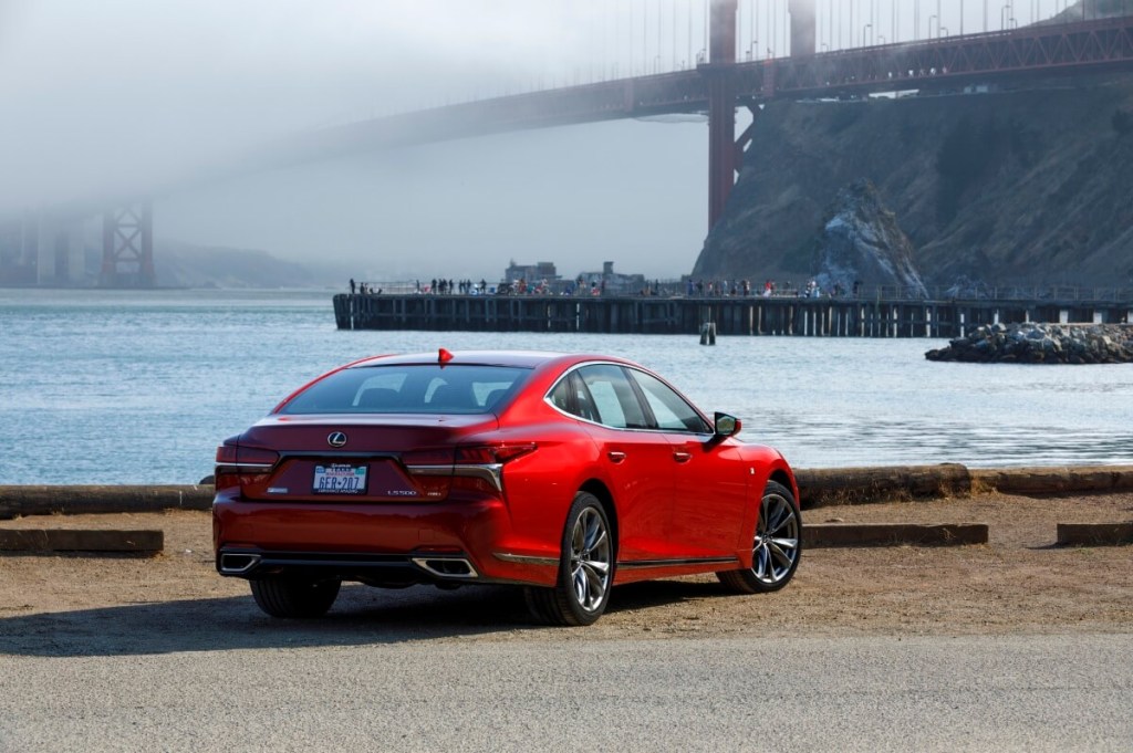 A red 2020 Lexus LS 500 luxury car shows off its rear-end styling by a waterfront. 