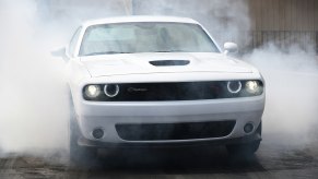 A white Dodge Challenger, one of the cheapest muscle cars on the market, does a burnout.