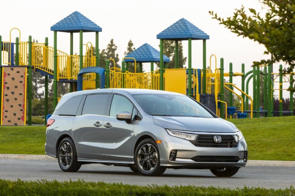 A silver Honda Odyssey parked in front of a public park. 