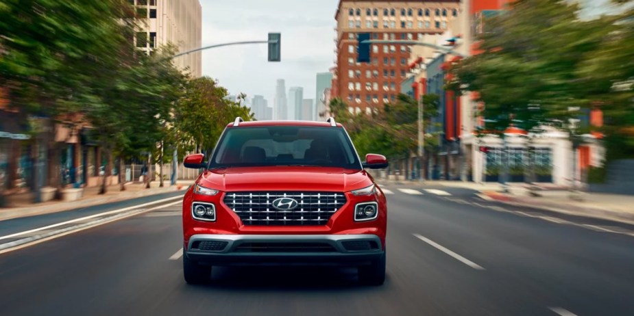 A red 2023 Hyundai Venue subcompact SUV is driving on the road. 