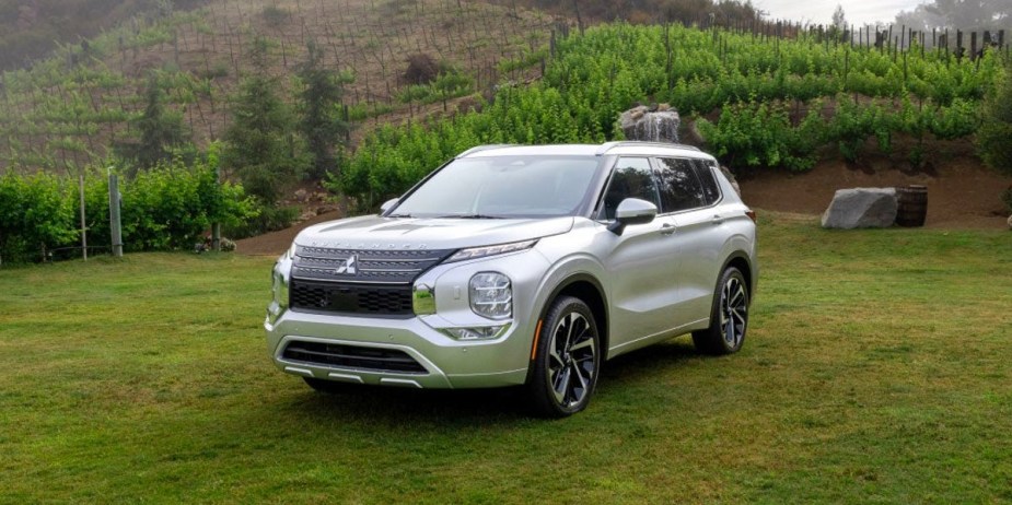 A white 2023 Mitsubishi Outlander midsize SUV is parked on the grass. 