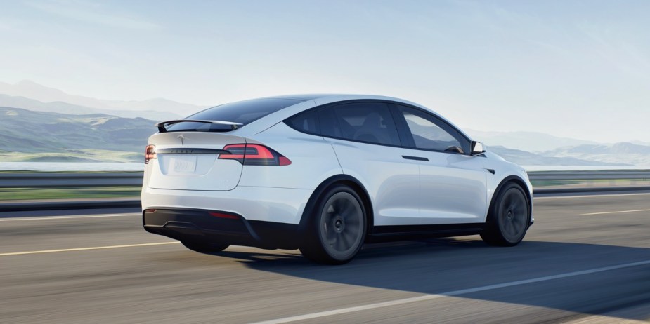 A white 2023 Tesla Model X midsize SUV is driving on the road. 