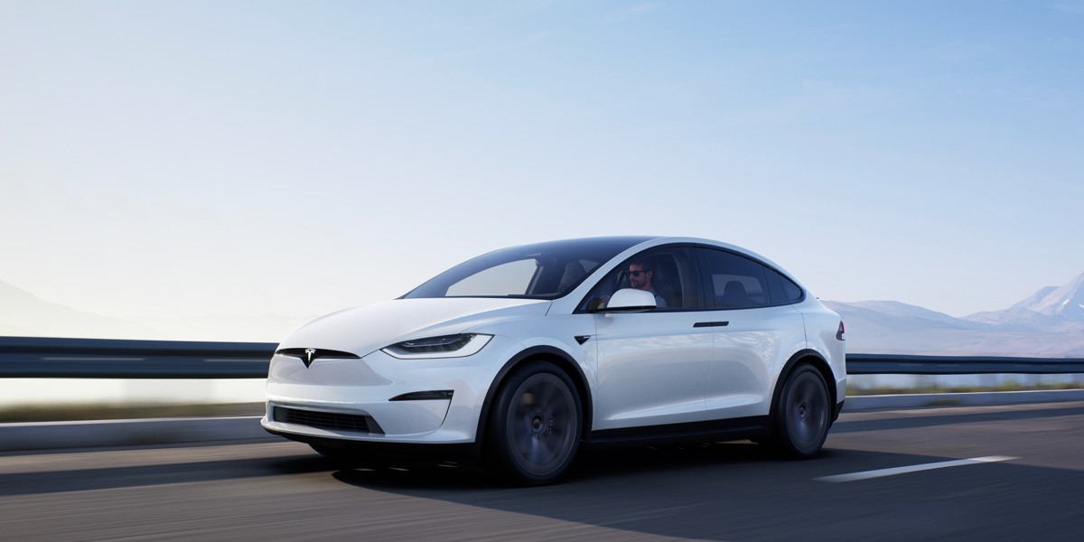 A white Tesla Model X midsize SUV is driving.