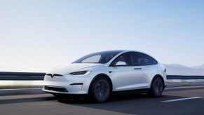 A white Tesla Model X midsize SUV is driving.