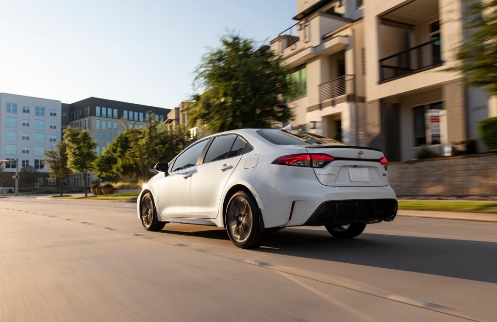 A white 2023 Toyota Corolla Hybrid, a capable AWD car and daily driver, drives on a city street. 