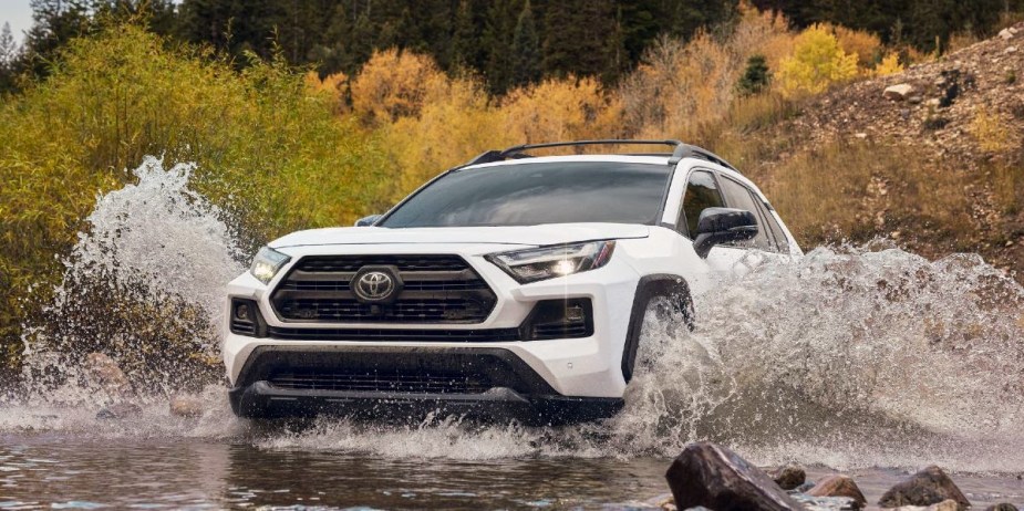 A white Toyota RAV4 small SUV is driving through the water. 