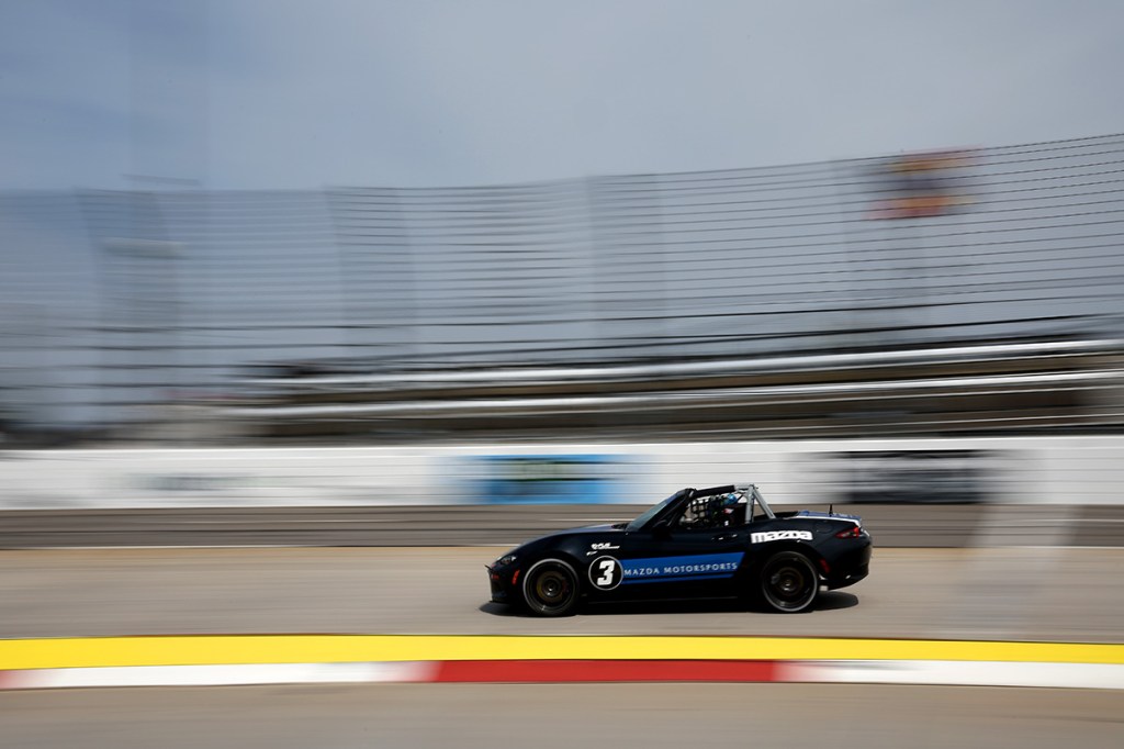 Black 2023 Mazda Miata MX-5 Cup Car blitzing down a race track in the U.S. with a blurred background due to its high performance specs