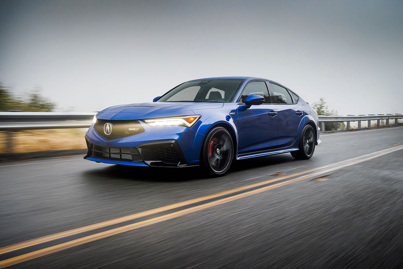 A 2024 Acura Integra in blue speeding down a roadway. The Acura Integra's price is pretty fair.