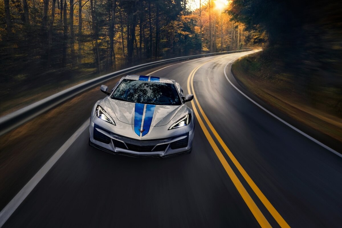 A silver and blue fully loaded 2024 Chevrolet Corvette E-Ray cruises around a corner.