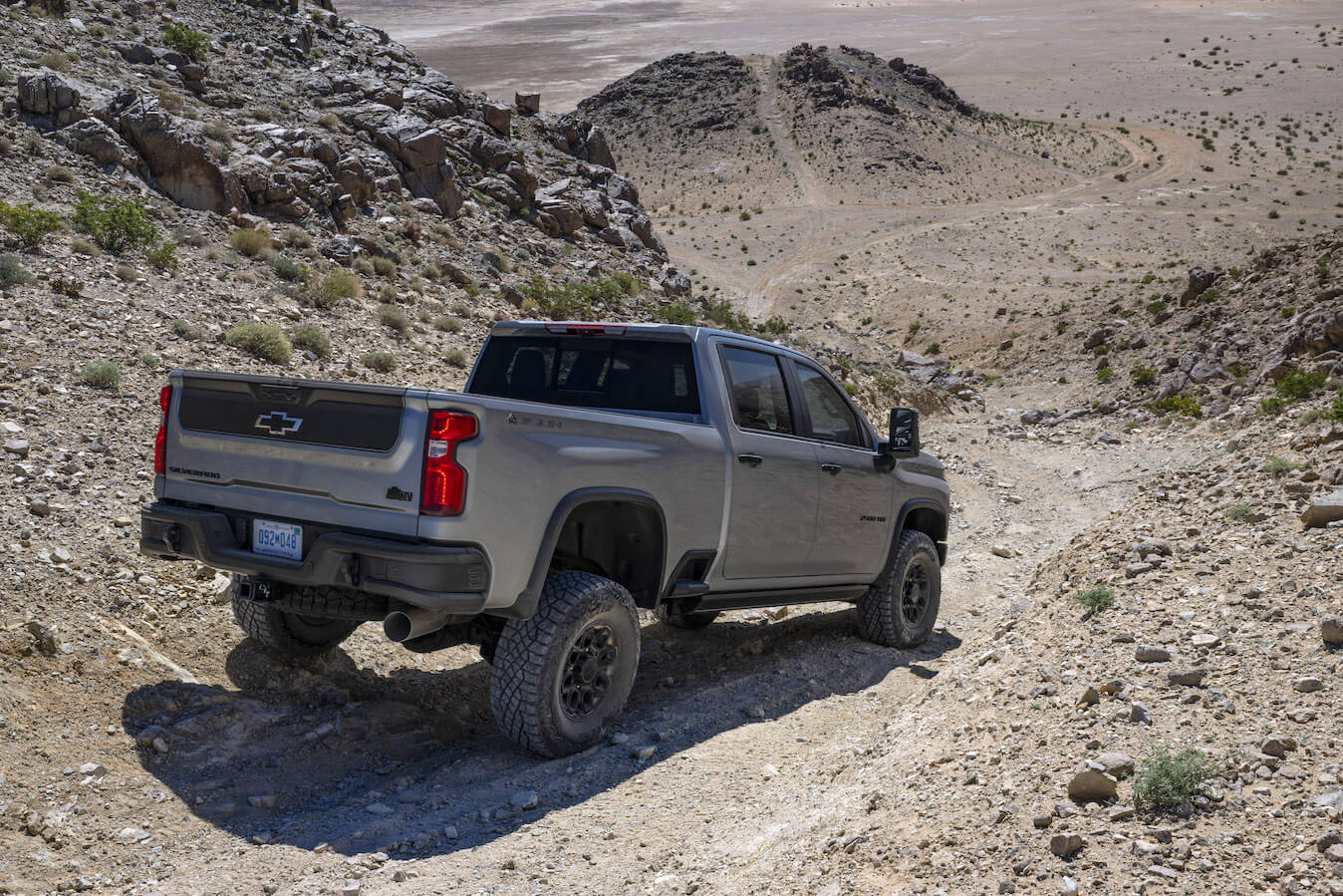 A silver 2024 Chevy Silverado HD driving down a dusty trail. Silverado HD dependability is a plus point.