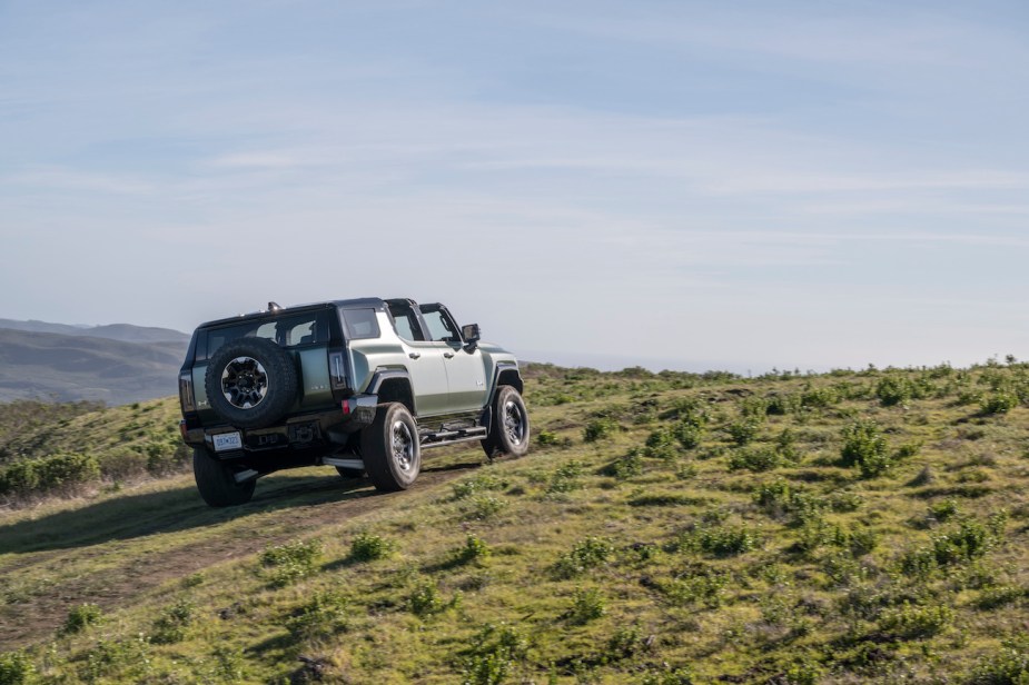Rear passenger-side shot of the 2024 GMC HUMMER EV SUV in Moonshot Green Matte with Sky Panels removed climbing a grassy off-road hill. GMC Hummer EV sales are on the rise.