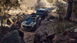 A 2024 Mazda CX-50 Meridian Edition compact off-road SUV model towing a camper near a river