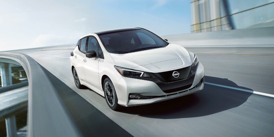 A white 2024 Nissan Leaf small electric car is driving on the road. 
