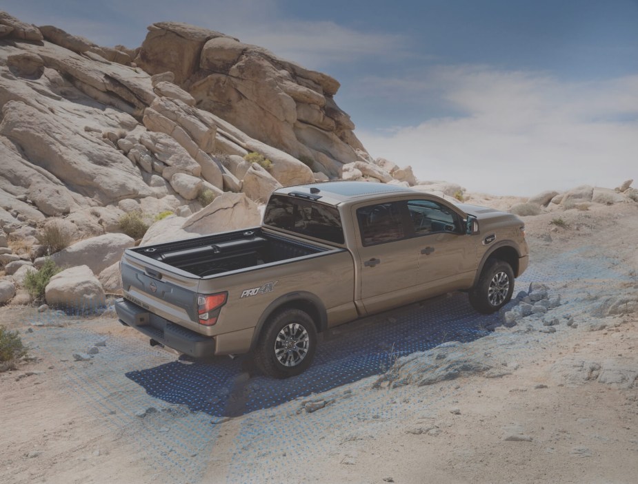 The bed of a beige Nissan Titan pickup truck driving up a steep, sand covered-hill in the desert. Rocks are visible in the background.