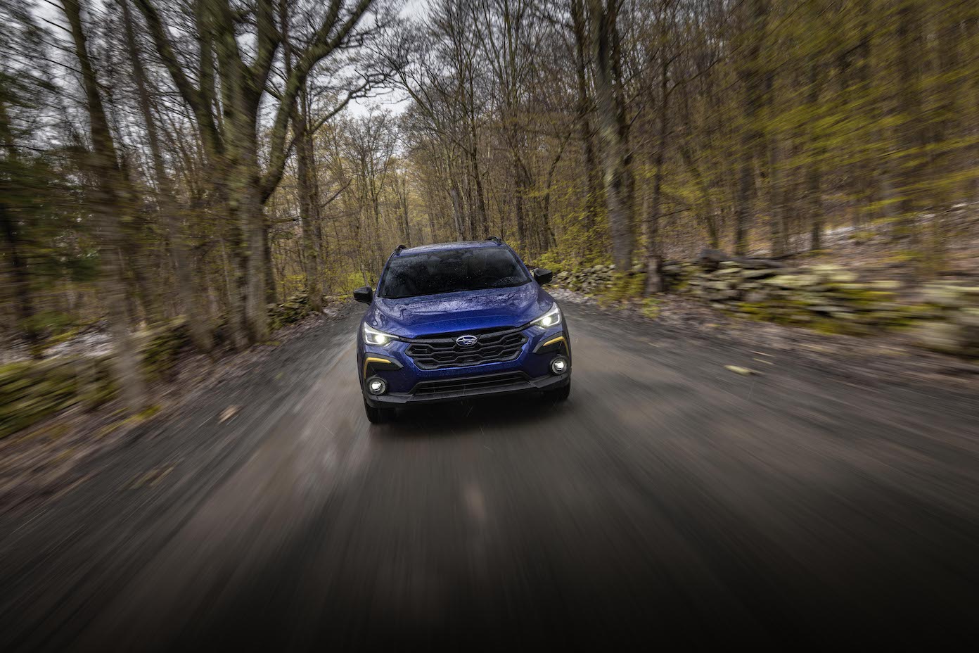 A blue 2024 Subaru Crosstrek driving down a forest road. Compare the 2024 Subaru Crosstrek vs. 2024 Jeep Compass.