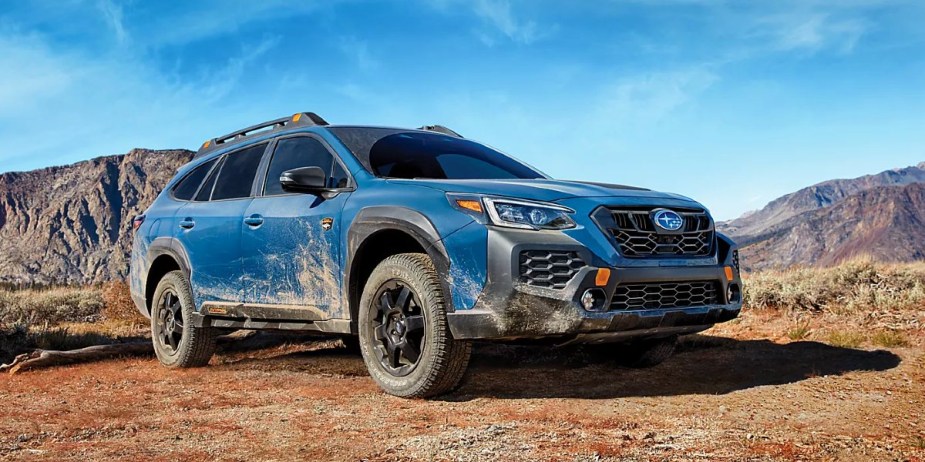 A blue 2024 Subaru Outback Wilderness midsize off-road SUV is driving off-road. 