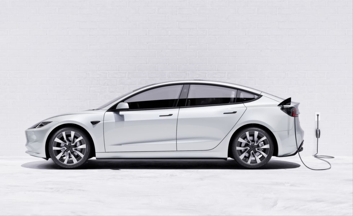 A new, white 2024 Tesla Model 3, with a new look and price, plugs into a charging station.